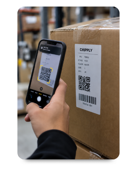 Close-up of a warehouse worker using a smartphone to scan a QR code on a shipping box to receive incoming apparel inventory.